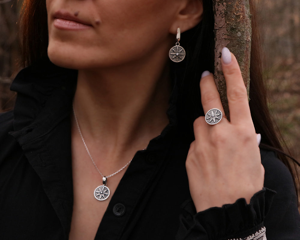 A woman wearing a sterling silver jewelry set consisting of a ring, necklace, and earrings with a geometric design, standing outdoors.