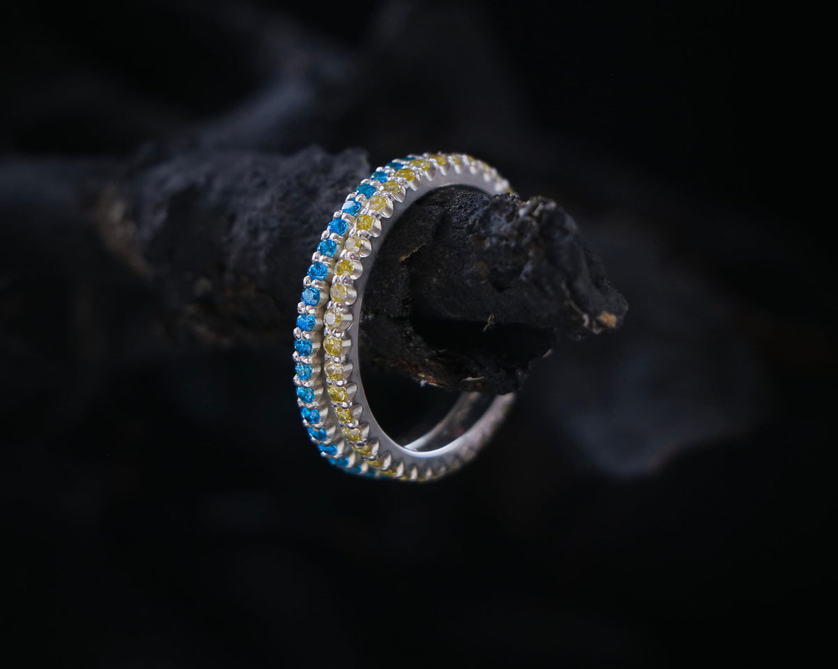 May include: A silver ring with a blue and yellow gemstone band.