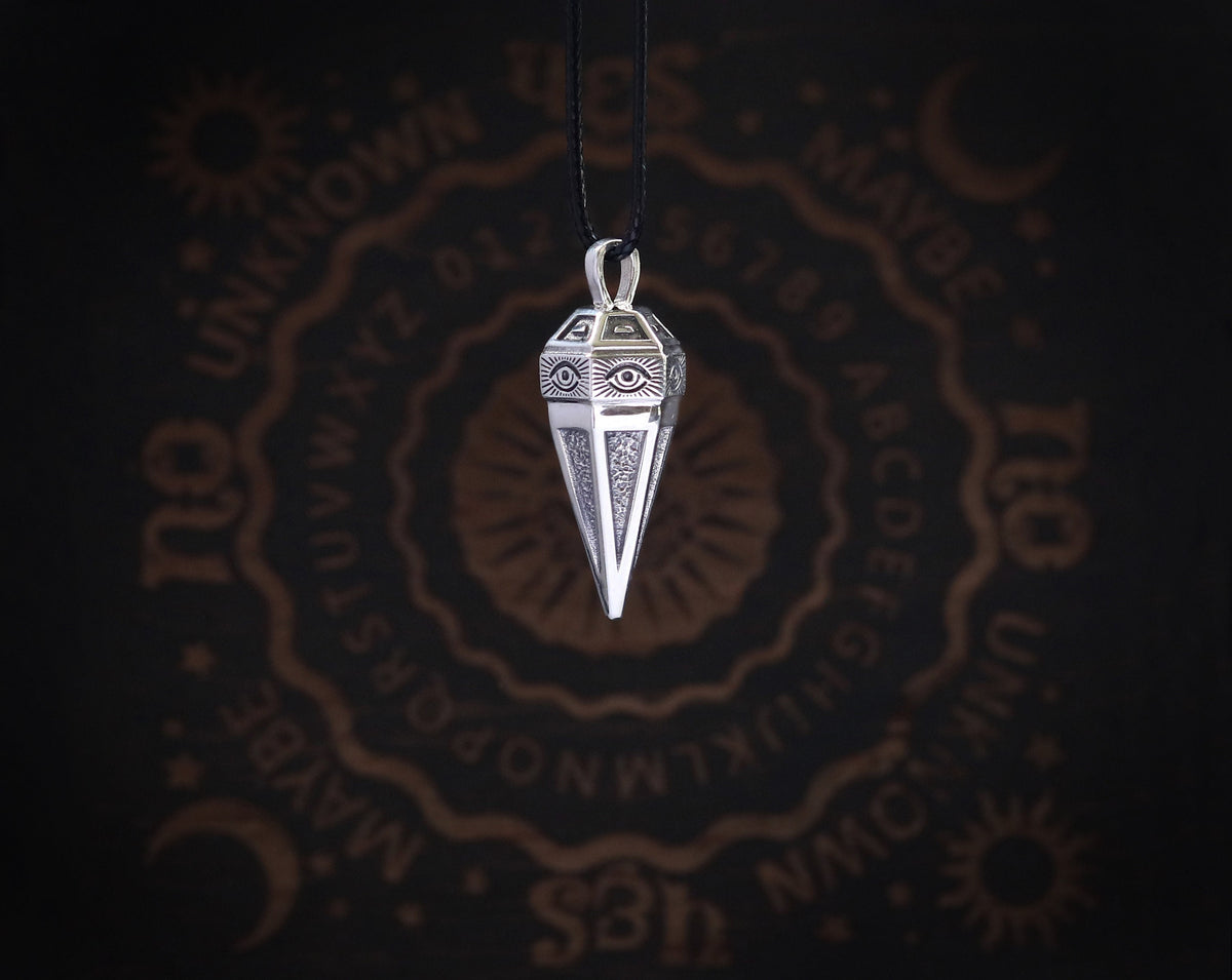 May include: Silver pendant necklace with a pyramid-shaped charm featuring an eye design. The charm is hanging from a black cord.