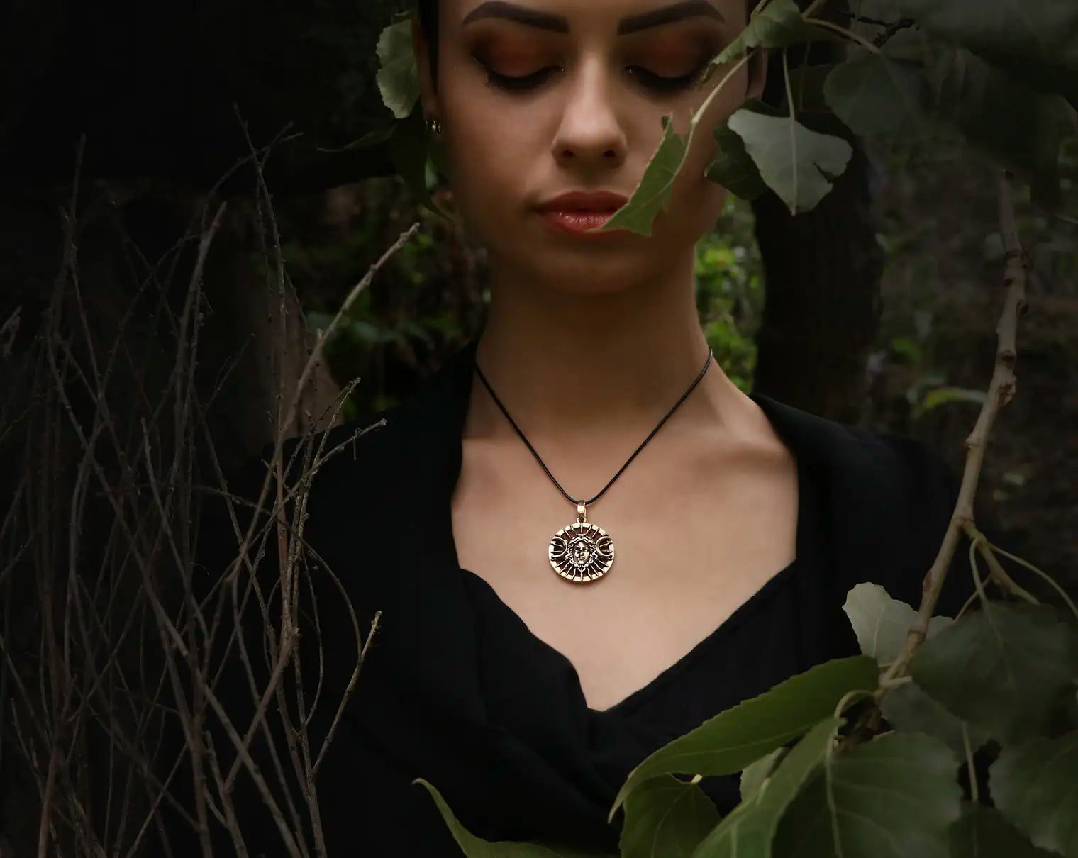 Woman wearing a Hecate necklace with a circular shape  in a dark, leafy setting