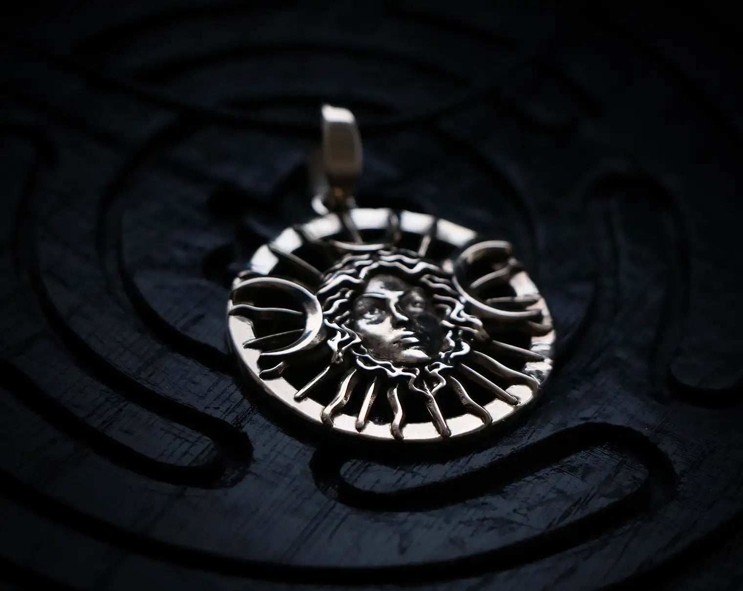 Silver Hecate pendant with face design on a dark background