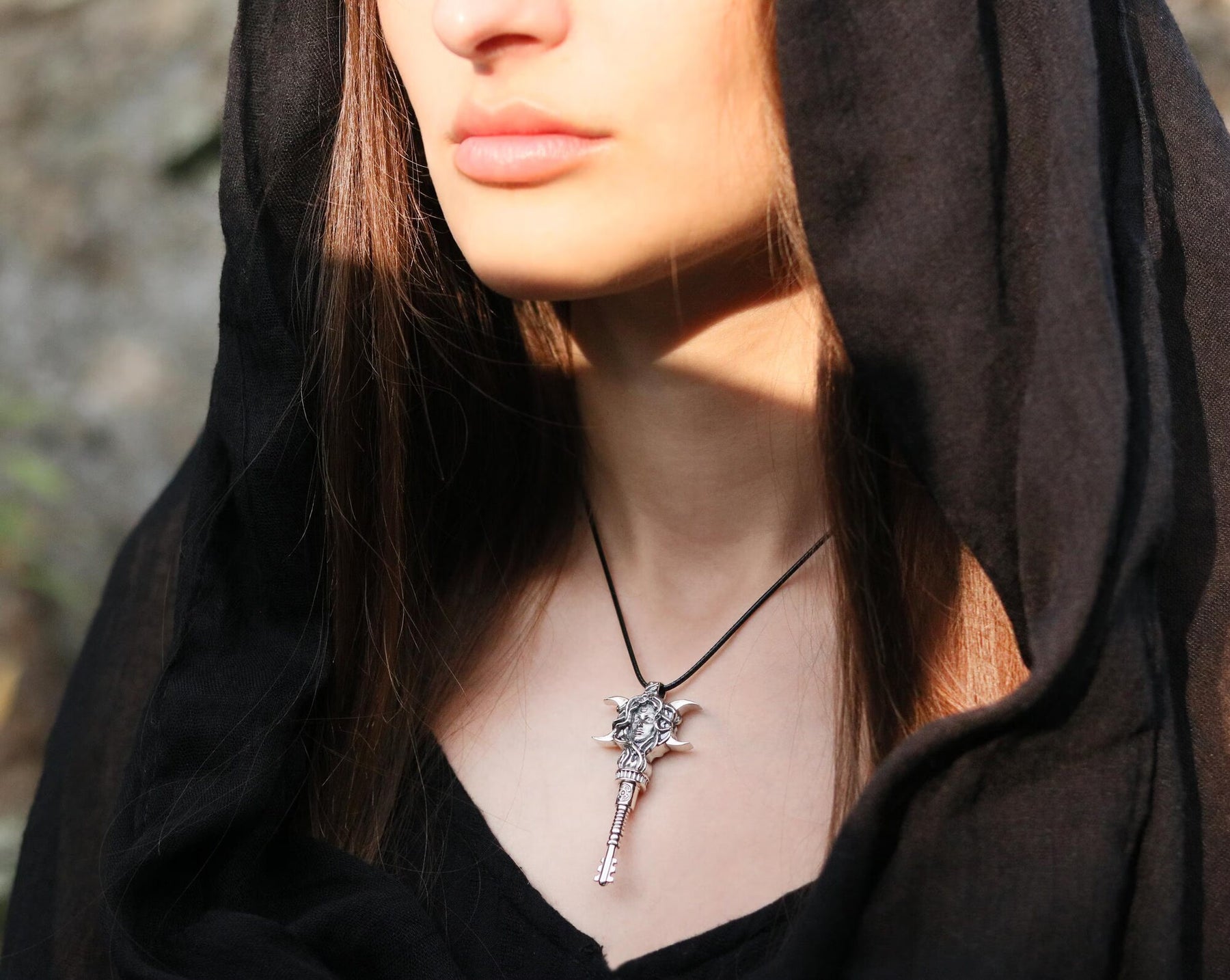 A close-up lifestyle shot of a woman wearing a black hooded cloak and a silver Hecate Key pendant necklace.