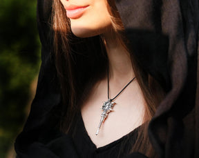 A close-up lifestyle shot of a woman wearing a detailed silver Hecate Key pendant necklace on a black cord, styled with a black hooded garment.