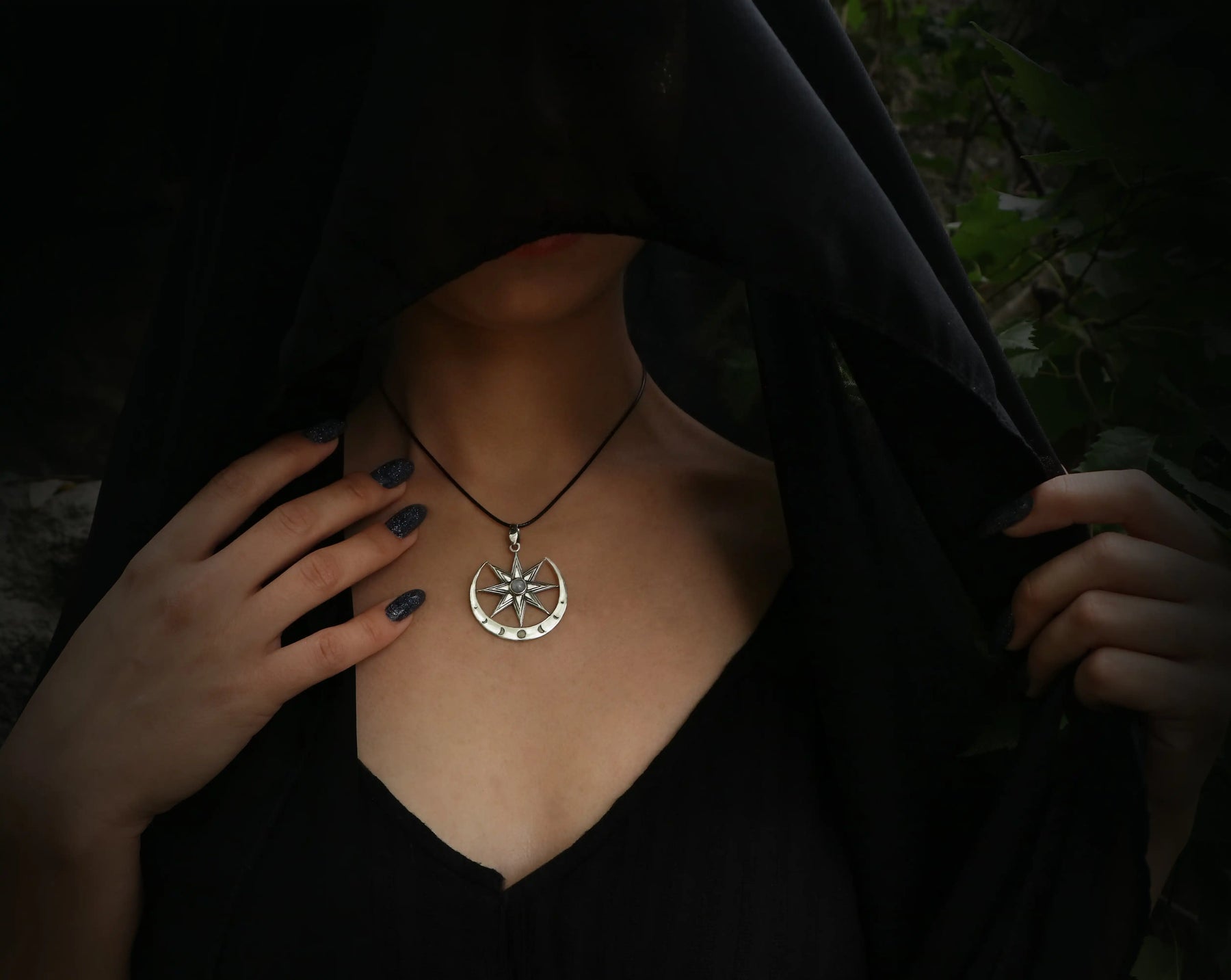 Person wearing a black hooded garment with a Inanna necklace featuring a moonstone