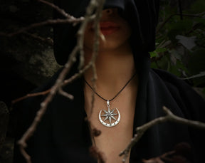 Person wearing a black hood with a Inanna necklace with moonstone in a dark, natural setting.