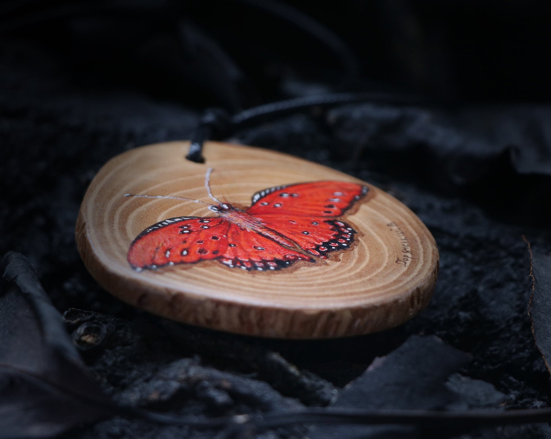 May include: A wooden pendant with a hand-painted red butterfly. The pendant is round and has a natural wood grain. The butterfly has black markings and is set against a light brown background.