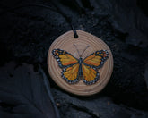May include: A wooden pendant with a hand-painted monarch butterfly design. The pendant is round and has a black cord.