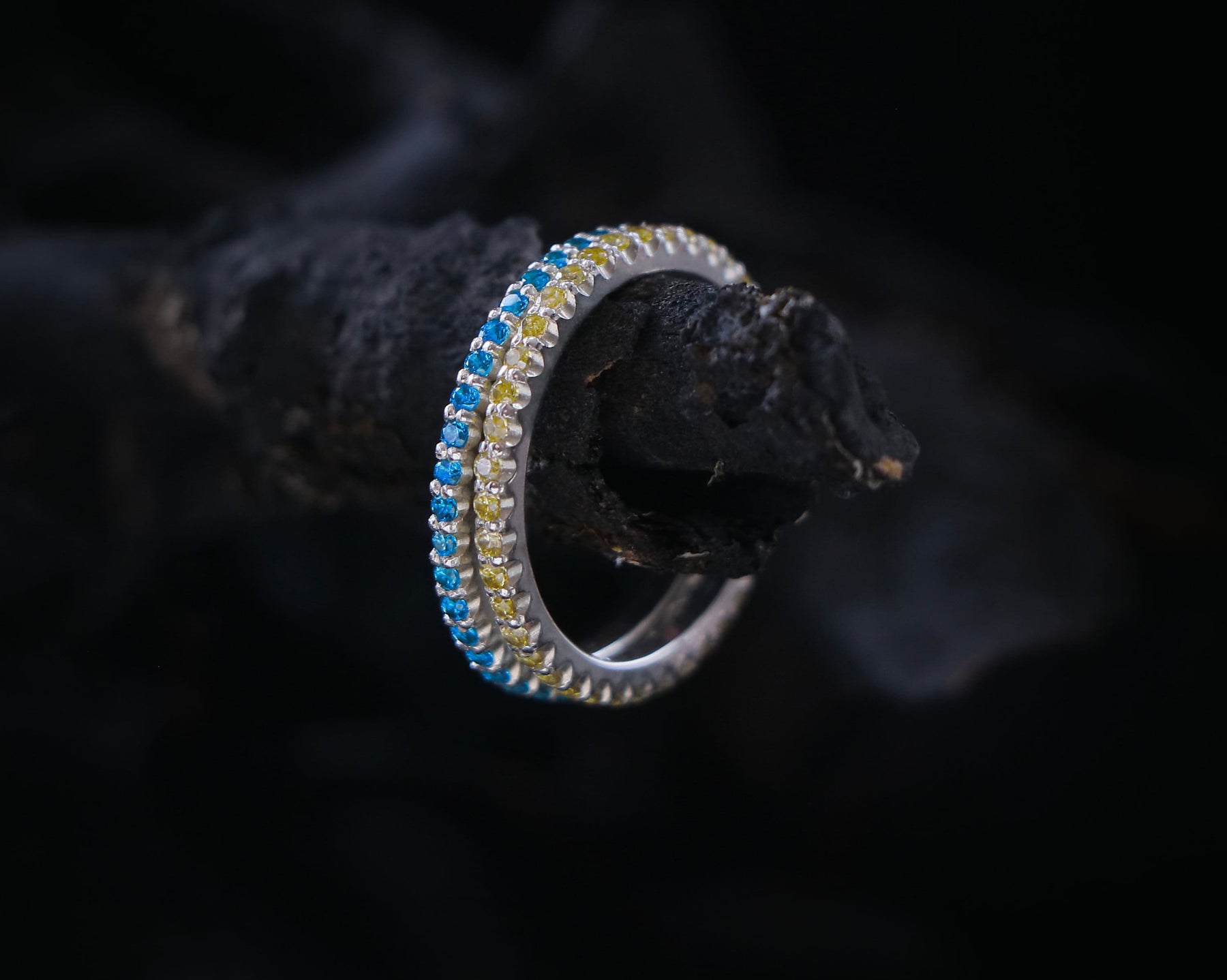 May include: A silver ring with a blue and yellow gemstone band.