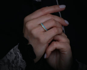 May include: A gold and blue ring with a textured design. The ring is worn on a finger.