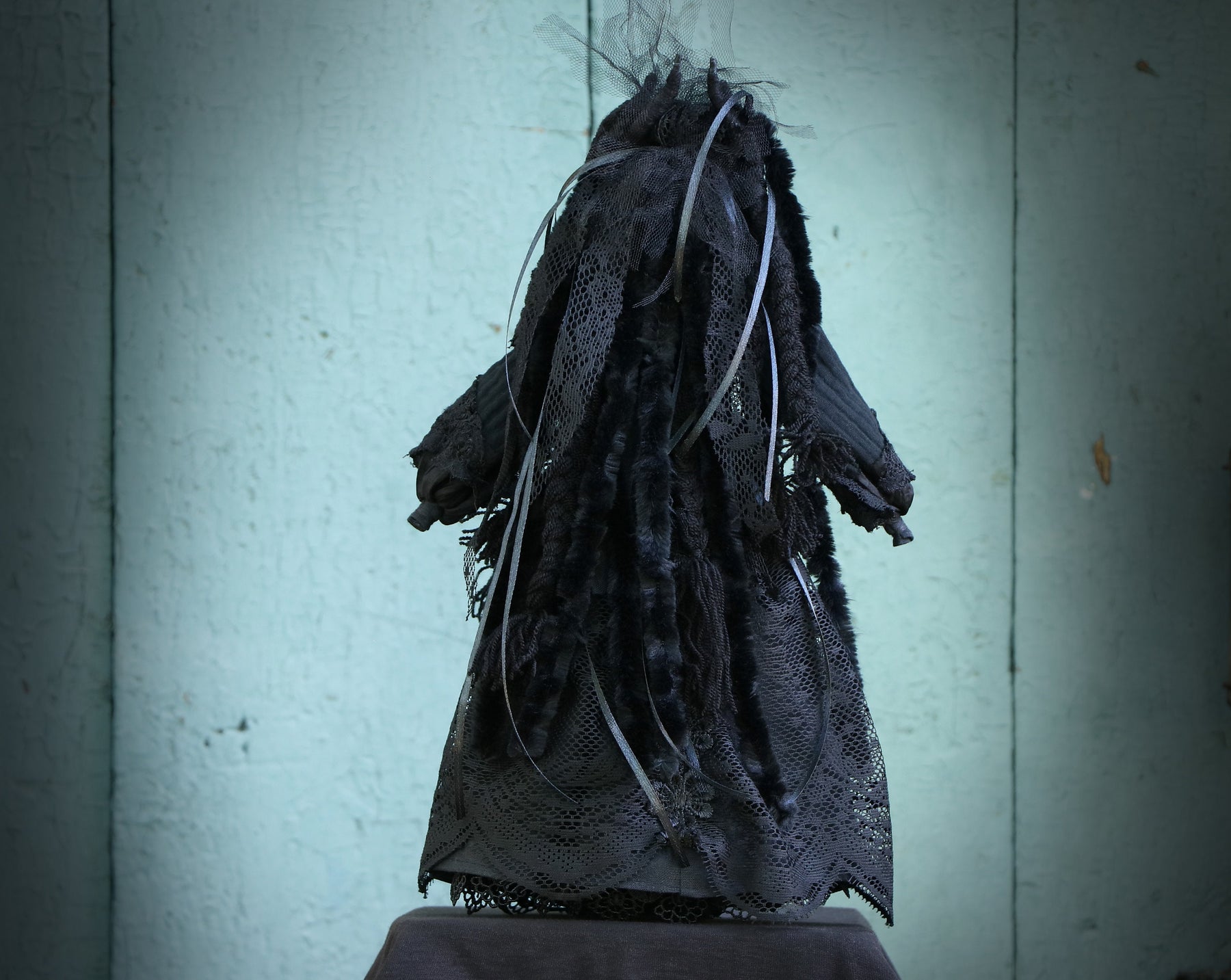 May include: A black doll with long, dark hair and a black lace dress. The doll is wearing a black veil and has a distressed, vintage look.