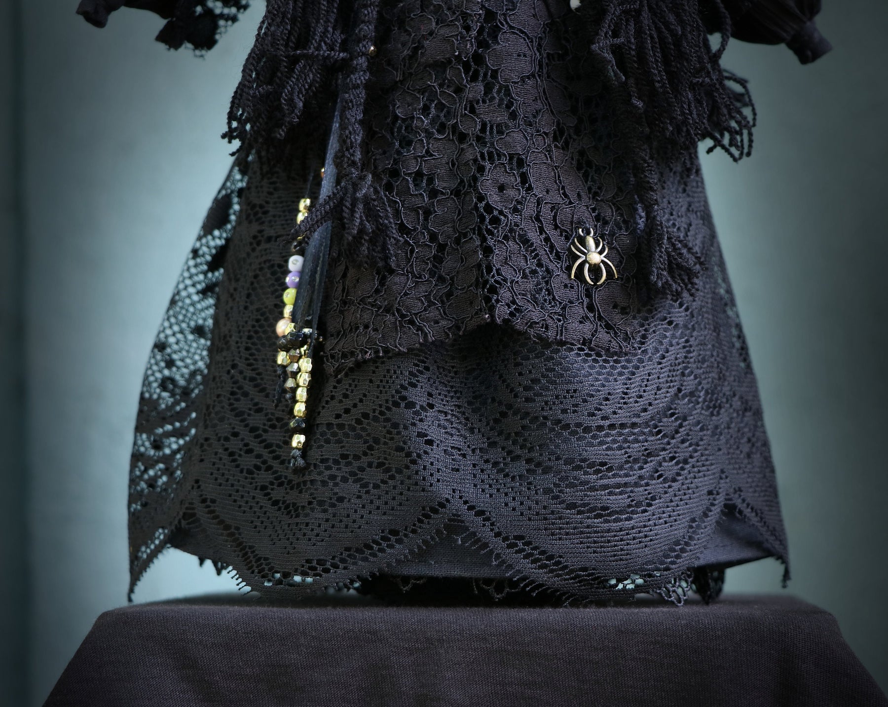 May include: Black lace dress with a spider brooch and beaded trim.