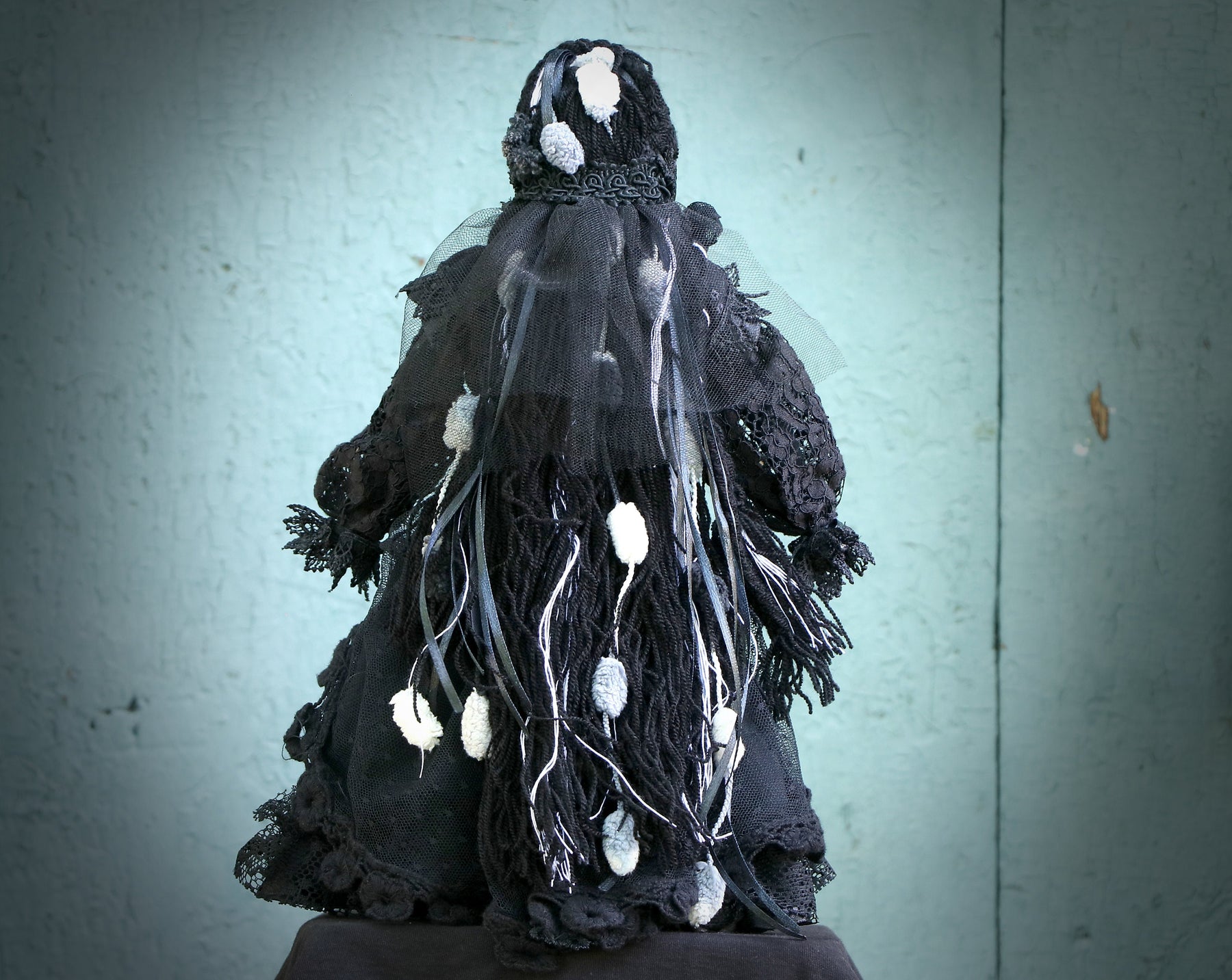 May include: A black and white doll wearing a black lace dress with white accents. The doll is dressed in a gothic style and has a veil over its head.