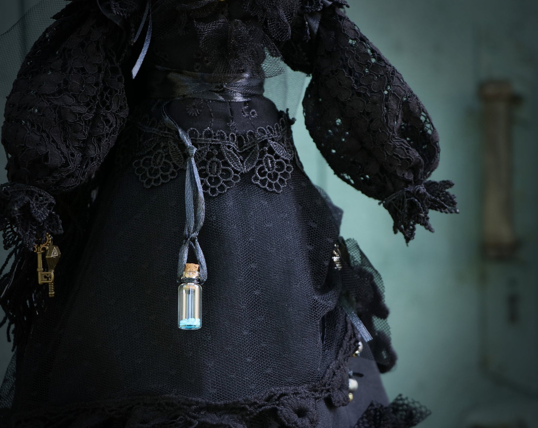 May include: A black lace dress with a small glass bottle hanging from a ribbon. The bottle contains a blue liquid.