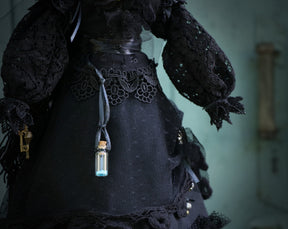 May include: A black lace dress with a small glass bottle hanging from a ribbon. The bottle contains a blue liquid.
