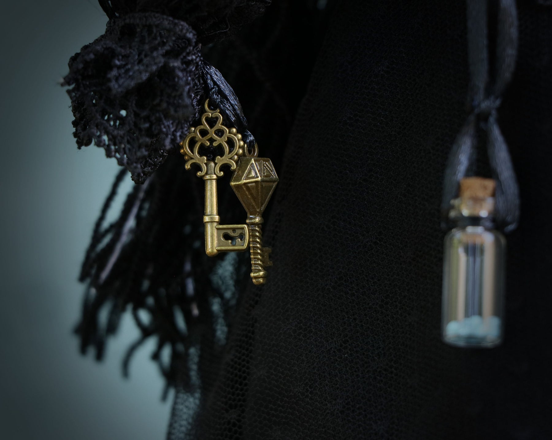 May include: A black lace fabric with a gold key charm and a small glass bottle with a cork stopper.