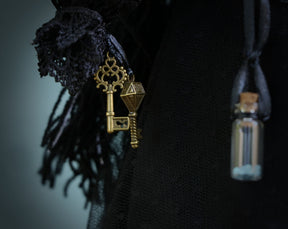 May include: A black lace fabric with a gold key charm and a small glass bottle with a cork stopper.