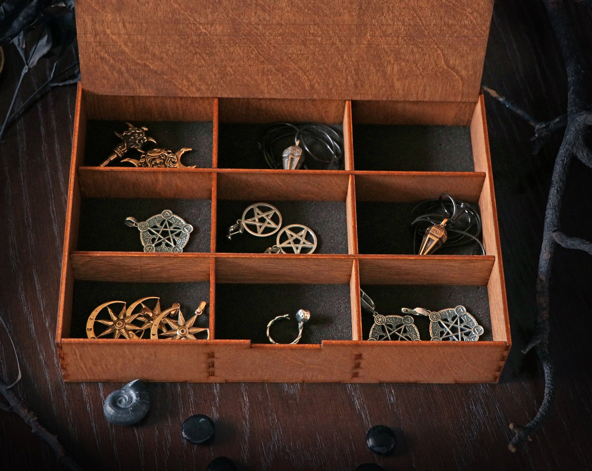 May include: A wooden box with nine compartments, each containing a different silver or gold pendant. The pendants feature various designs, including stars, moons, and other symbols.