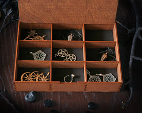 May include: A wooden box with nine compartments, each containing a different silver or gold pendant. The pendants feature various designs, including stars, moons, and other symbols.