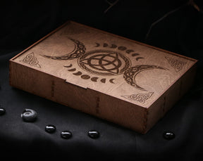 May include: A wooden box with a triple moon and triquetra design engraved on the lid. The box is made of dark wood and has a natural finish.