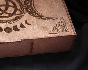 May include: A wooden box with a Celtic knot design and a crescent moon pattern. The box is made of dark brown wood and has a hinged lid.