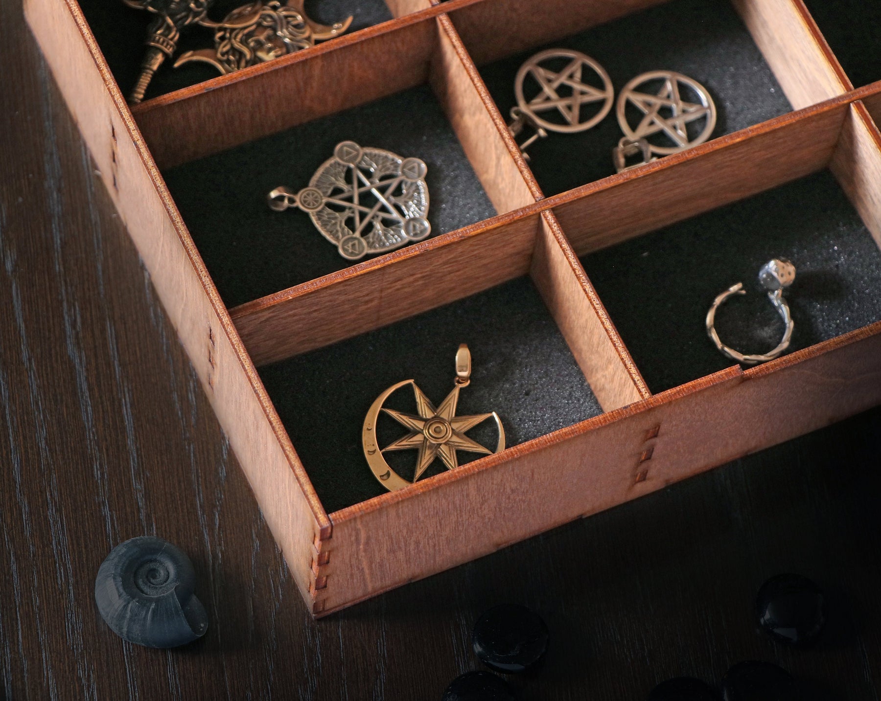 May include: A wooden box with compartments, each containing a different silver or gold pendant. The pendants feature various designs, including stars, circles, and other geometric shapes.