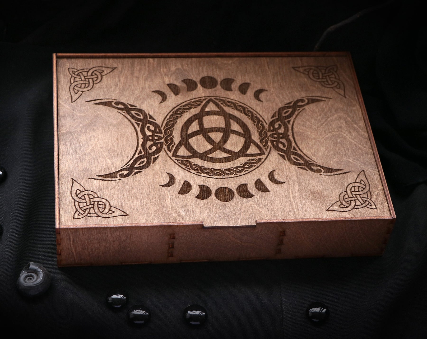 May include: A wooden box with a triple moon and triquetra design. The box is made of dark wood and has a hinged lid.