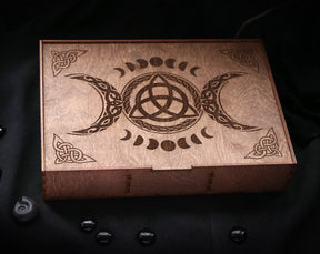 May include: A wooden box with a triple moon and triquetra design. The box is made of dark wood and has a hinged lid.