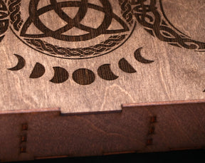 May include: A wooden box with a Celtic knot design and a series of crescent moons carved into the top. The box has a dark brown stain.
