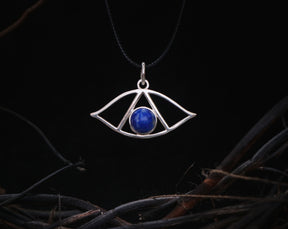 May include: A silver pendant necklace with a blue lapis lazuli stone in the center, shaped like an eye. The pendant is hanging from a black cord.