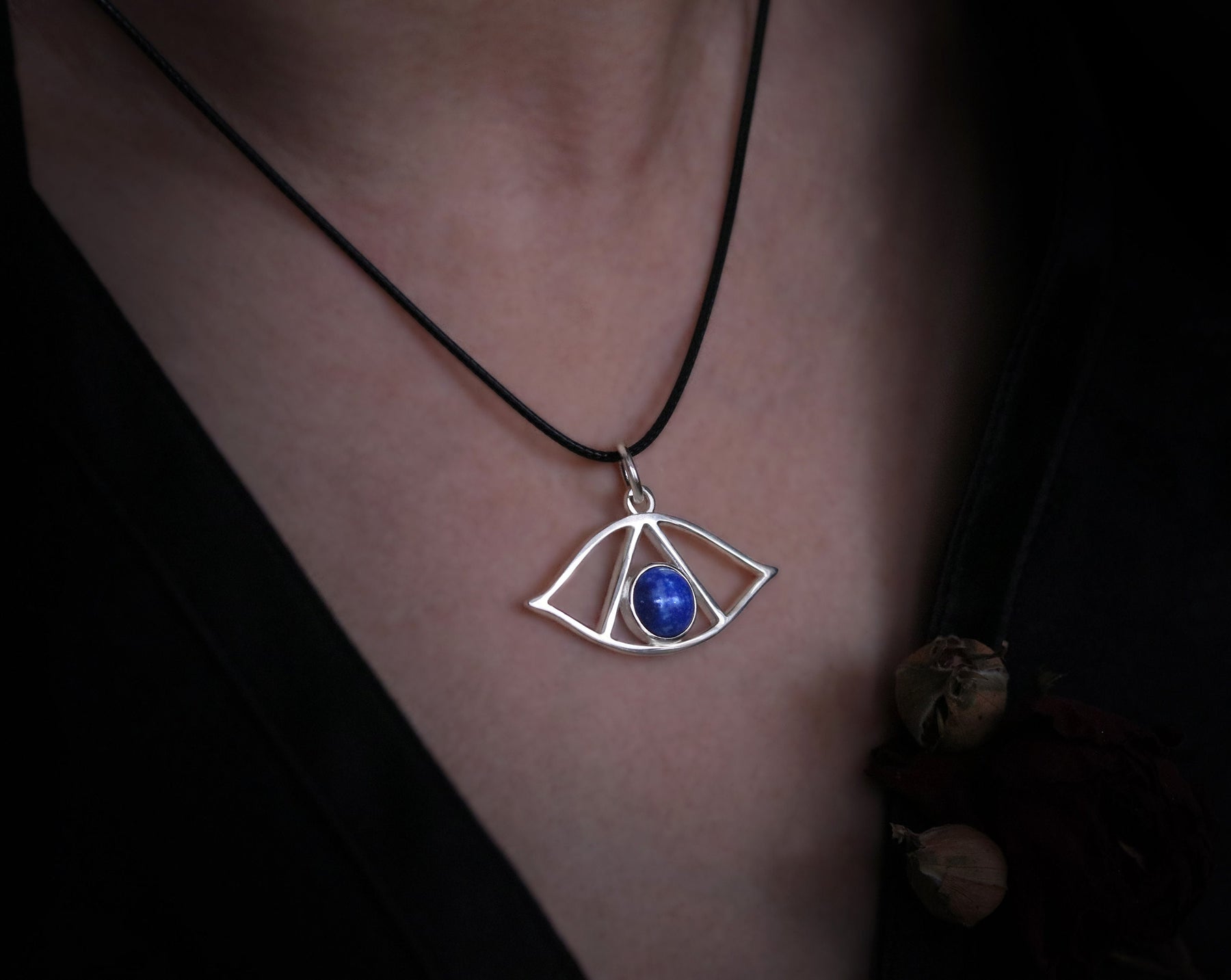 May include: A silver necklace with a pendant shaped like an eye with a blue lapis lazuli stone in the center.