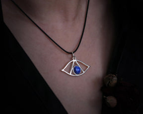 May include: A silver necklace with a pendant shaped like an eye with a blue lapis lazuli stone in the center.