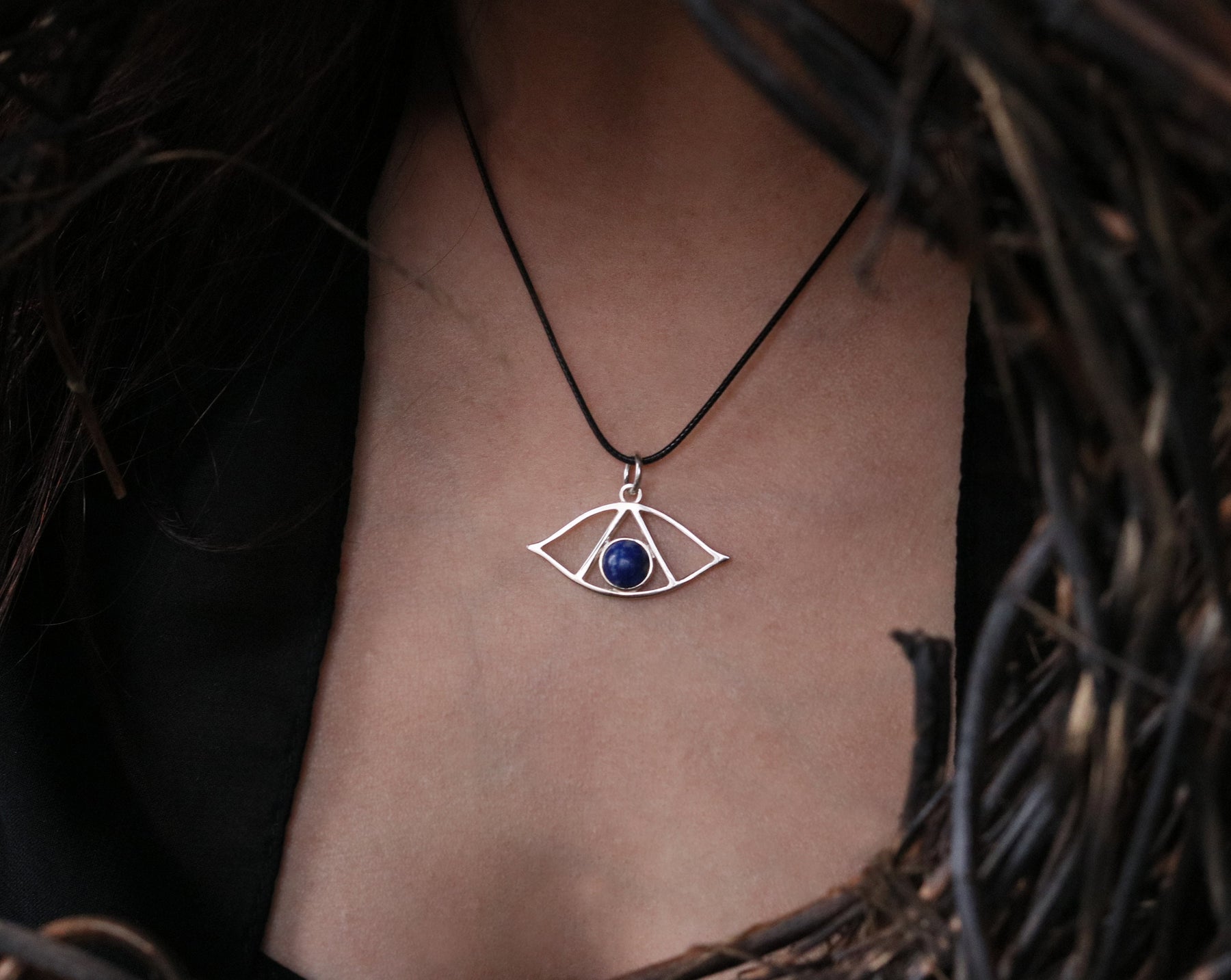 May include: A silver necklace with a geometric eye pendant featuring a blue lapis lazuli stone.