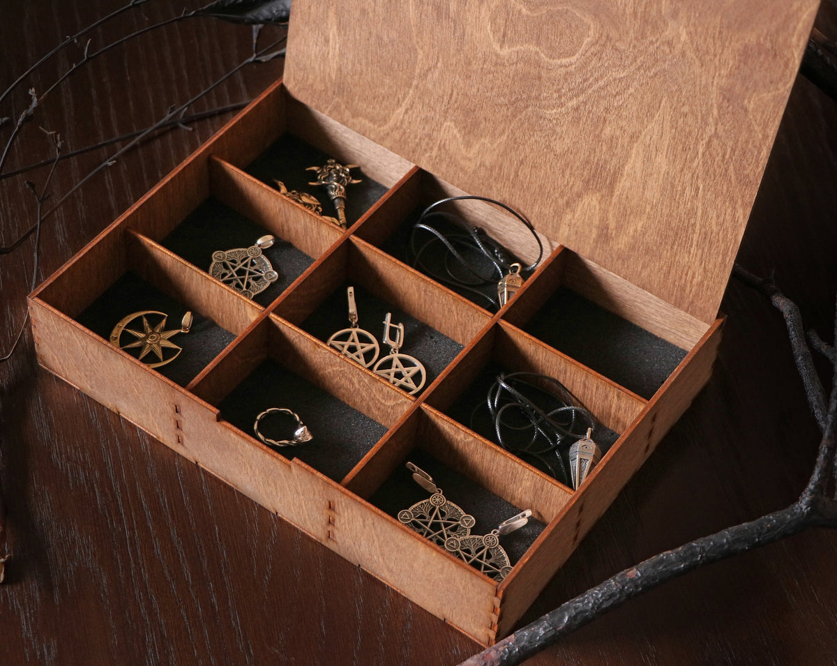 May include: A wooden box with nine compartments, each containing a different piece of jewelry. The jewelry includes earrings, pendants, and a compass. The box is made of dark wood and has a natural finish.
