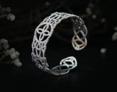 May include: A silver bracelet with a delicate, intricate design. The bracelet is made of a thin metal and has a rounded shape.