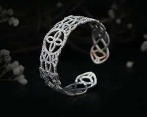 May include: A silver bracelet with a delicate, intricate design. The bracelet is made of a thin metal and has a rounded shape.