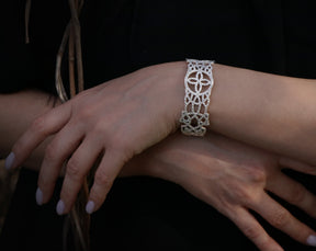 May include: A silver bracelet with a delicate, intricate design. The bracelet is made of small, interconnected pieces that create a floral pattern.