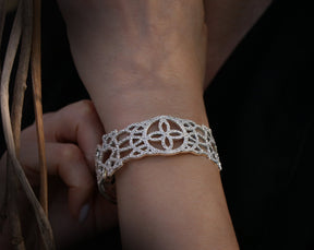 May include: A silver bracelet with a delicate, intricate design featuring a repeating pattern of small circles and flowers. The bracelet is made of metal and is adorned with sparkling stones.