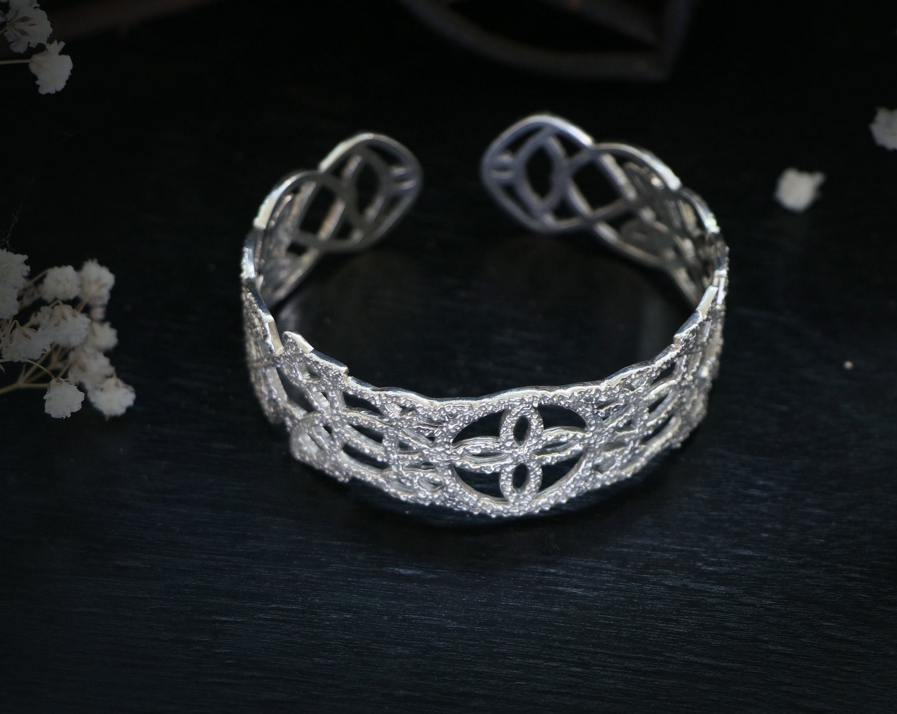 May include: A silver openwork cuff bracelet with a delicate, intricate design.
