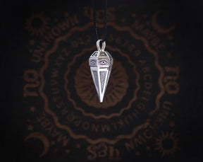 May include: Silver pendant necklace with a pyramid-shaped charm featuring an eye design. The charm is hanging from a black cord.