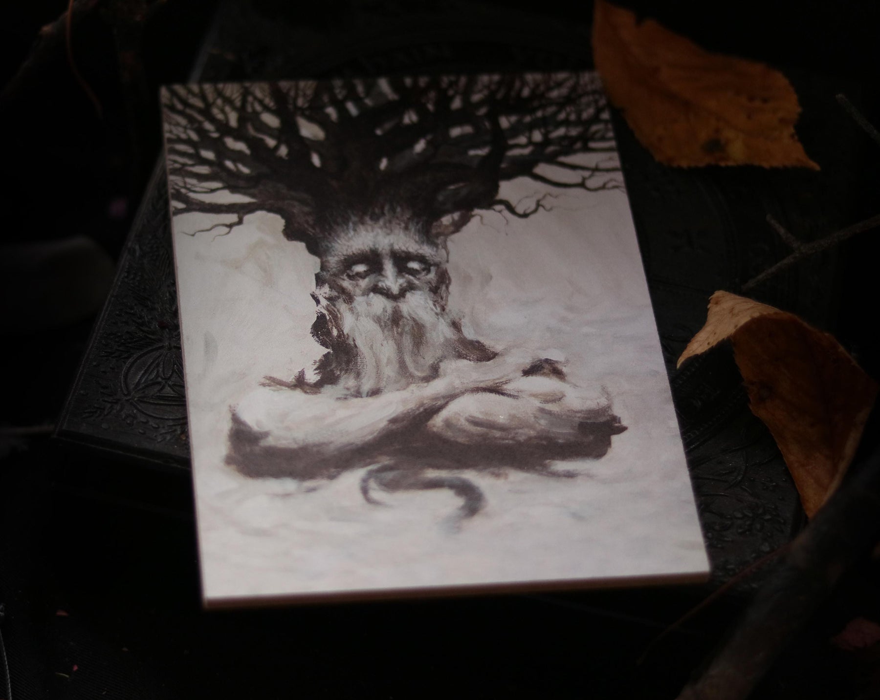 May include: A black and white illustration of a tree spirit with a large, gnarled tree growing from its head. The spirit has a long, white beard and is sitting with its arms crossed.