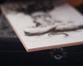 May include: A close-up of a wooden plaque with a light brown background and a black and white abstract design.