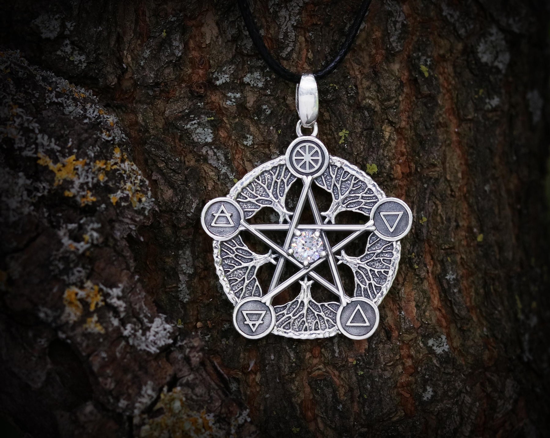 May include: Silver pendant necklace featuring a five-pointed star with a clear crystal in the center. The star is surrounded by five tree branches with symbols representing the elements: earth, air, fire, water, and spirit.