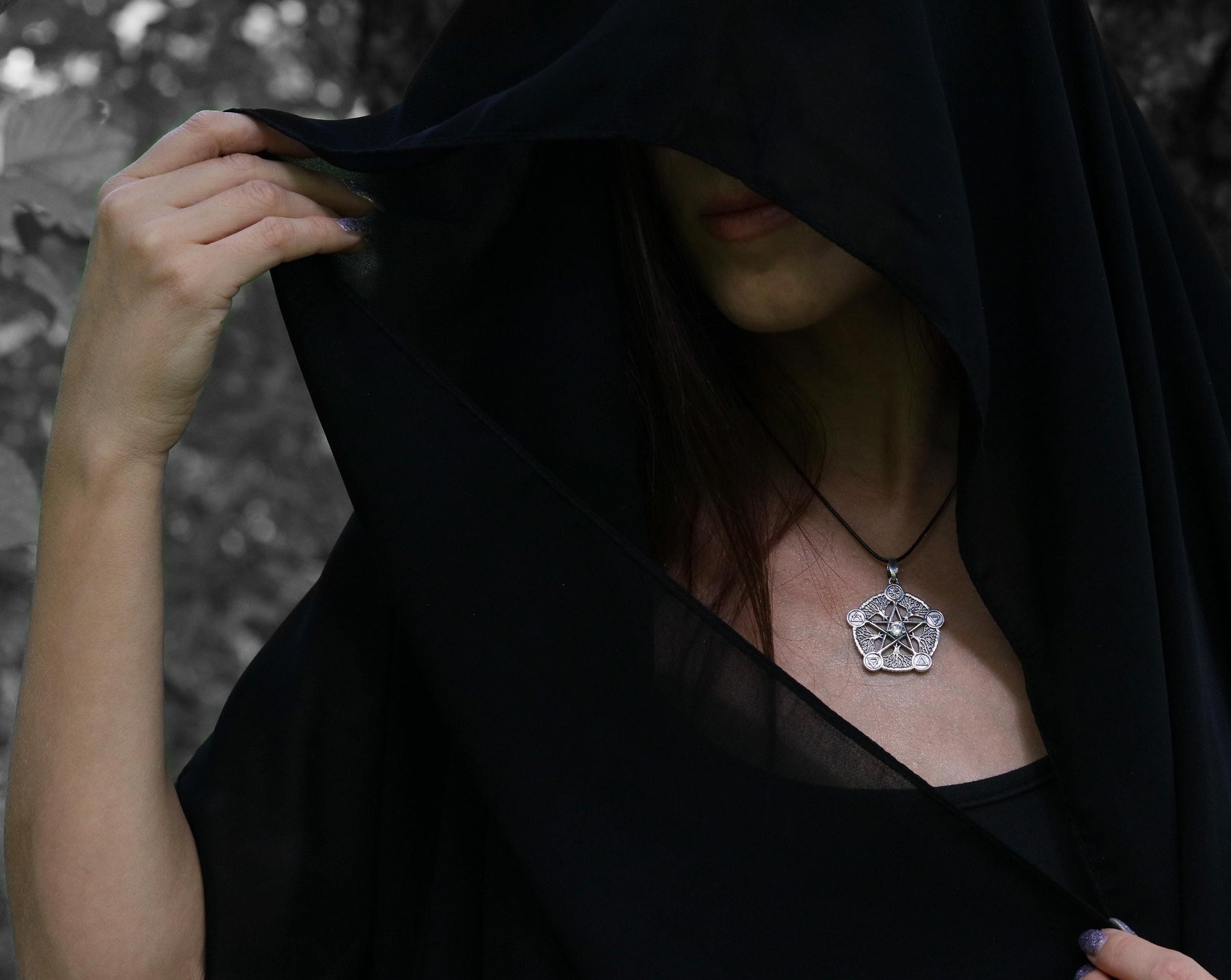 May include: A person wearing a black hooded cloak with a silver pendant necklace featuring a detailed geometric design.