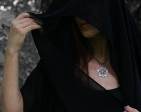 May include: A person wearing a black hooded cloak with a silver pendant necklace featuring a detailed geometric design.