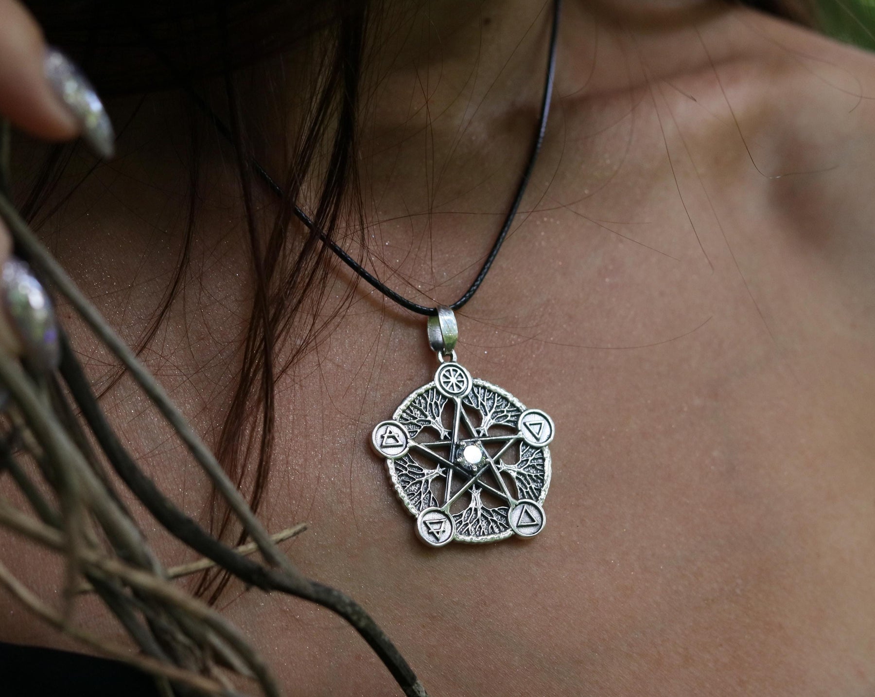 May include: A silver pendant necklace with a five-pointed star design. The star is surrounded by five smaller symbols, each representing a different element. The pendant is on a black cord.