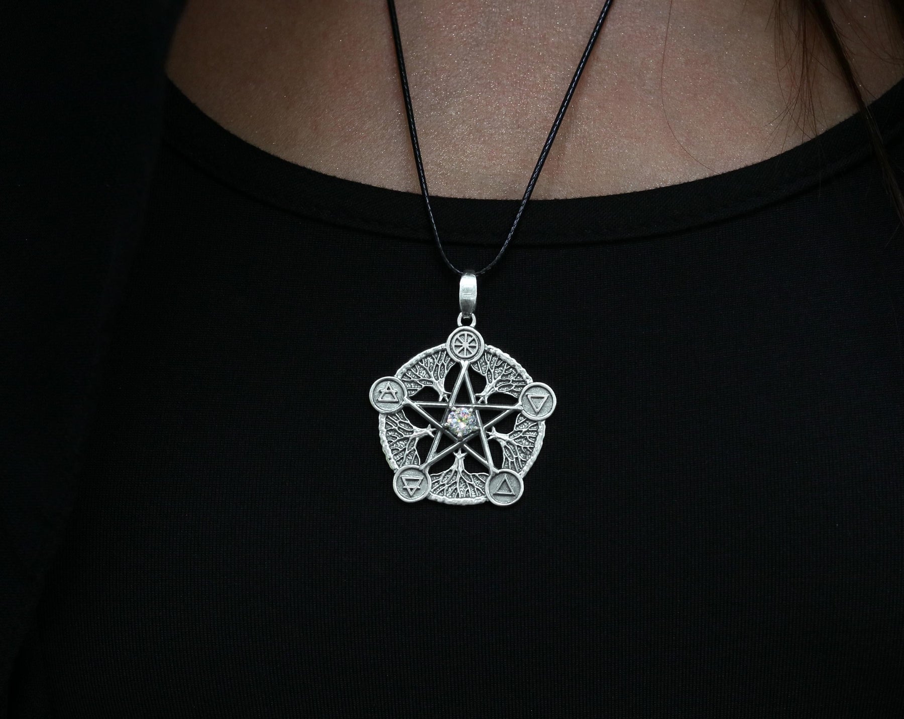 May include: A silver pendant necklace with a five-pointed star design. The star is surrounded by five smaller symbols, each representing a different element. The necklace is on a black cord.
