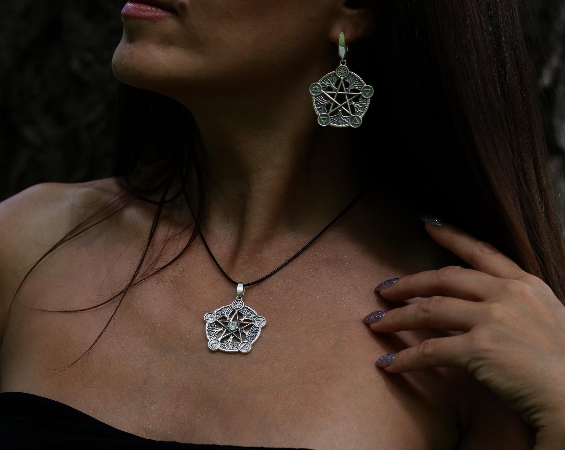 May include: A silver necklace and earrings with a pentacle design. The pentacle is a five-pointed star within a circle, and the necklace has a black cord.
