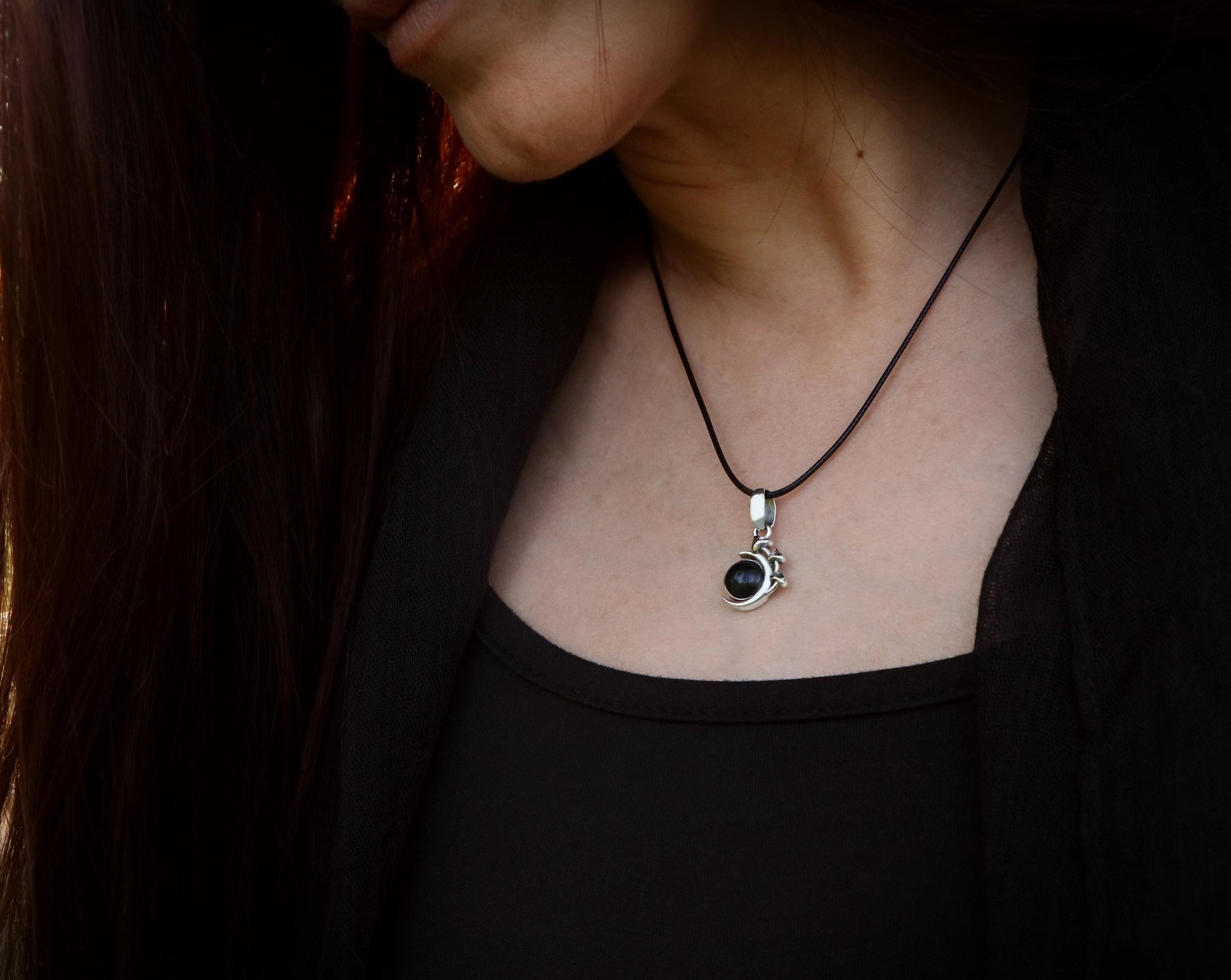 May include: A silver necklace with a black gemstone pendant. The pendant is a round, cabochon-cut stone set in a silver setting. The necklace is on a black cord.