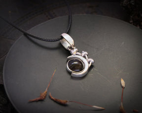May include: A silver pendant necklace with a dark gray gemstone set in a crescent moon design. The pendant is on a black cord.