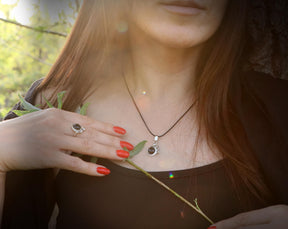 May include: A silver necklace with a black gemstone pendant in the shape of a crescent moon. The necklace is worn by a person with long brown hair and red nail polish.